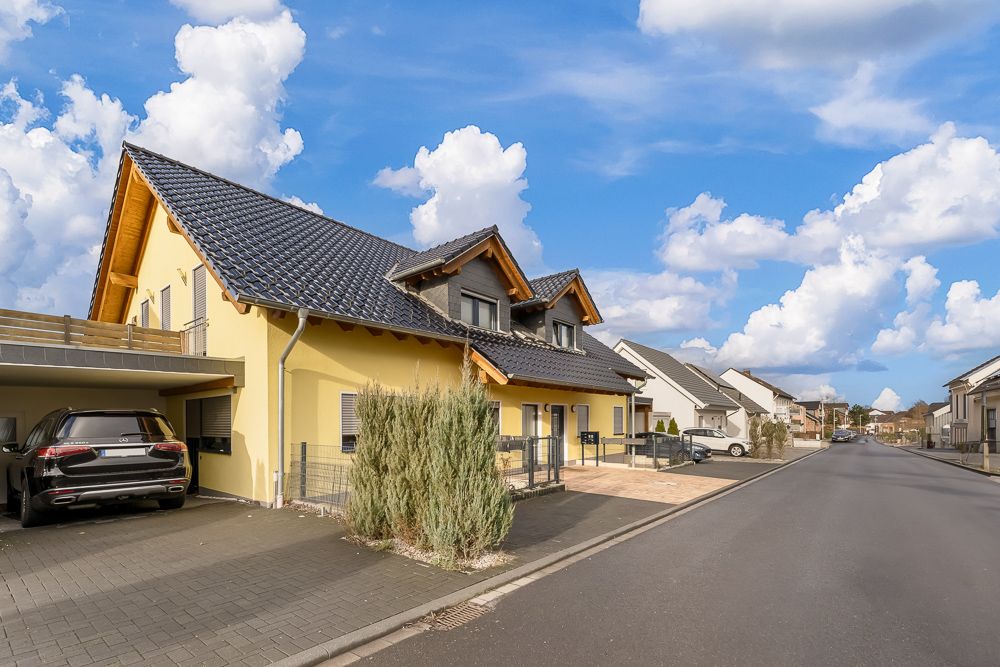 Gelbes Einfamilienhaus mit Carport und Auto in einer ruhigen Wohnstraße.