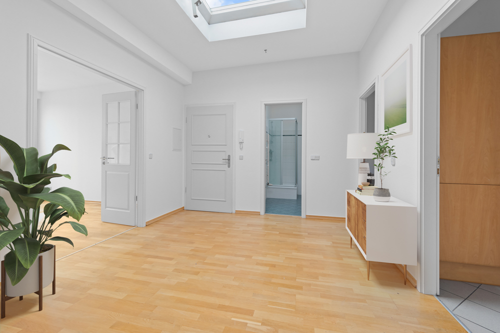 Heller Flur mit Holzfußboden, Pflanzen, Kommode und Deckenfenster.