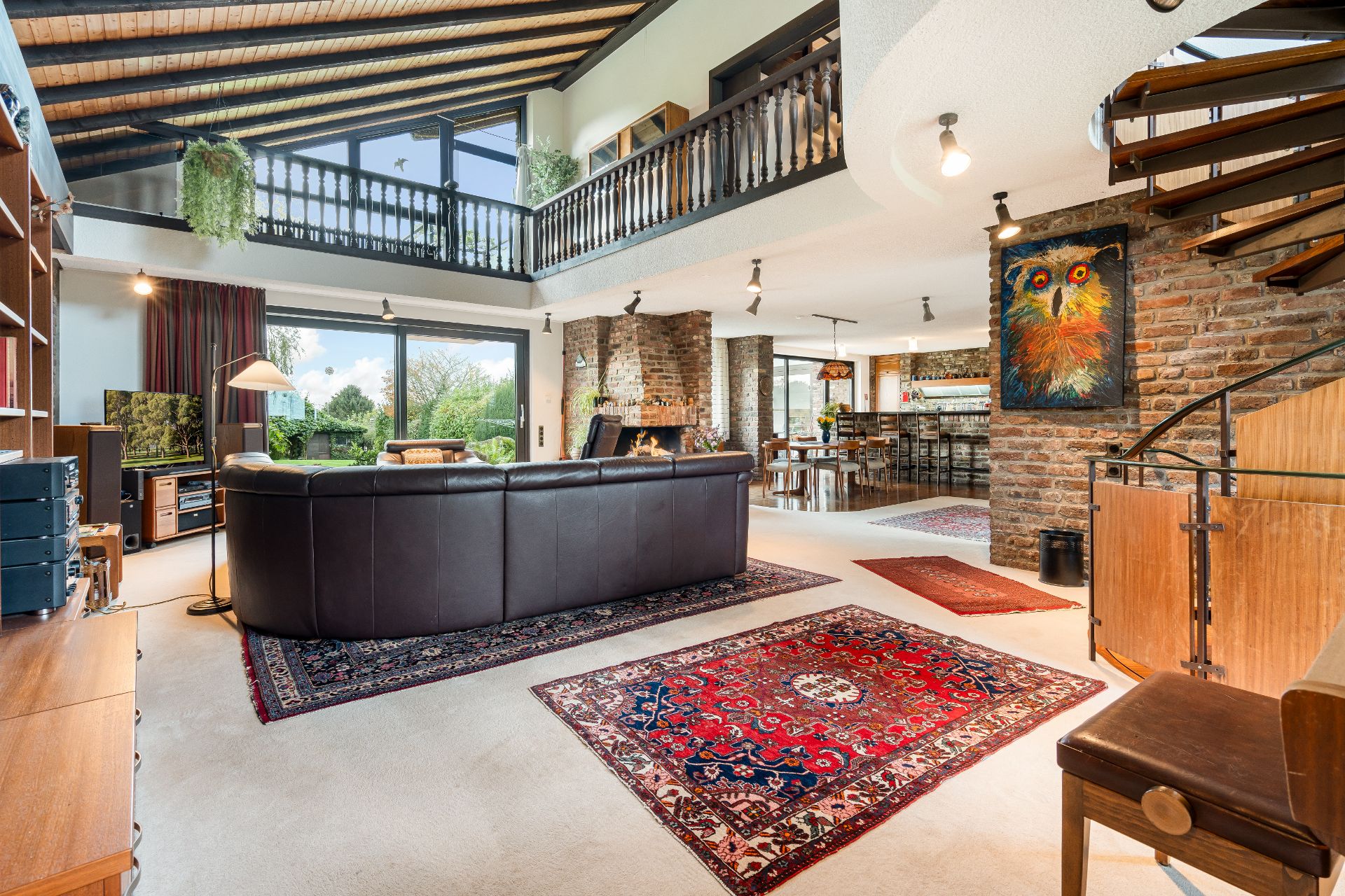 Großes Wohnzimmer mit Ledersofa, bunten Teppichen, Kamin und Treppe, moderne Einrichtung, viel Tageslicht.