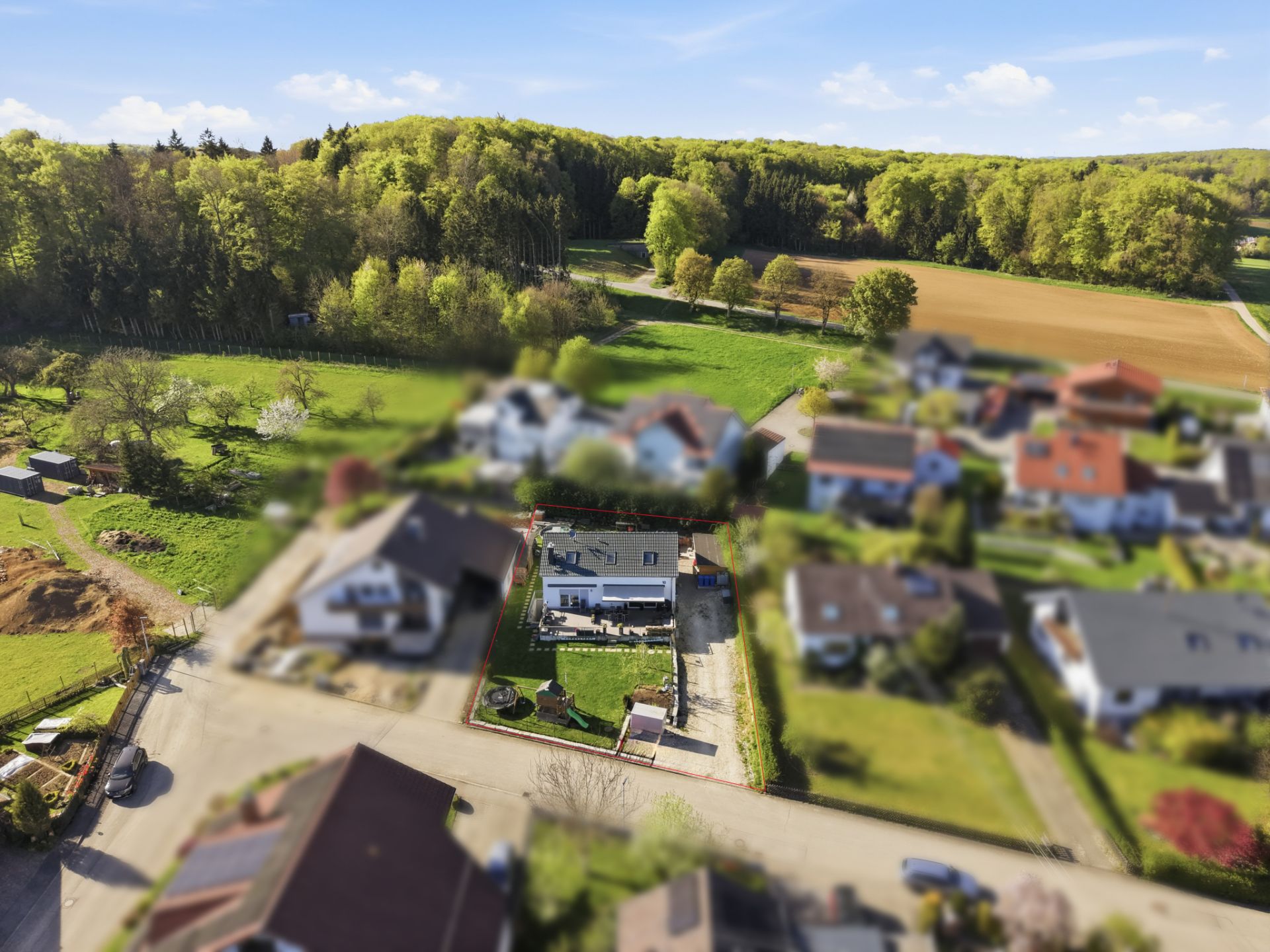 Luftaufnahme eines Wohnhauses mit Garten, umgeben von weiteren Häusern und viel Grün.
