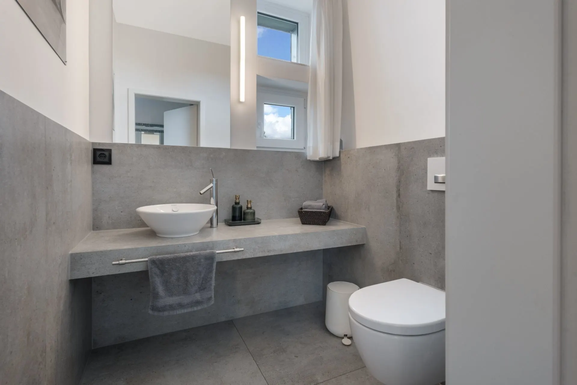 Modernes Badezimmer mit Waschbecken, Spiegel, Toilette und grauen Fliesen.