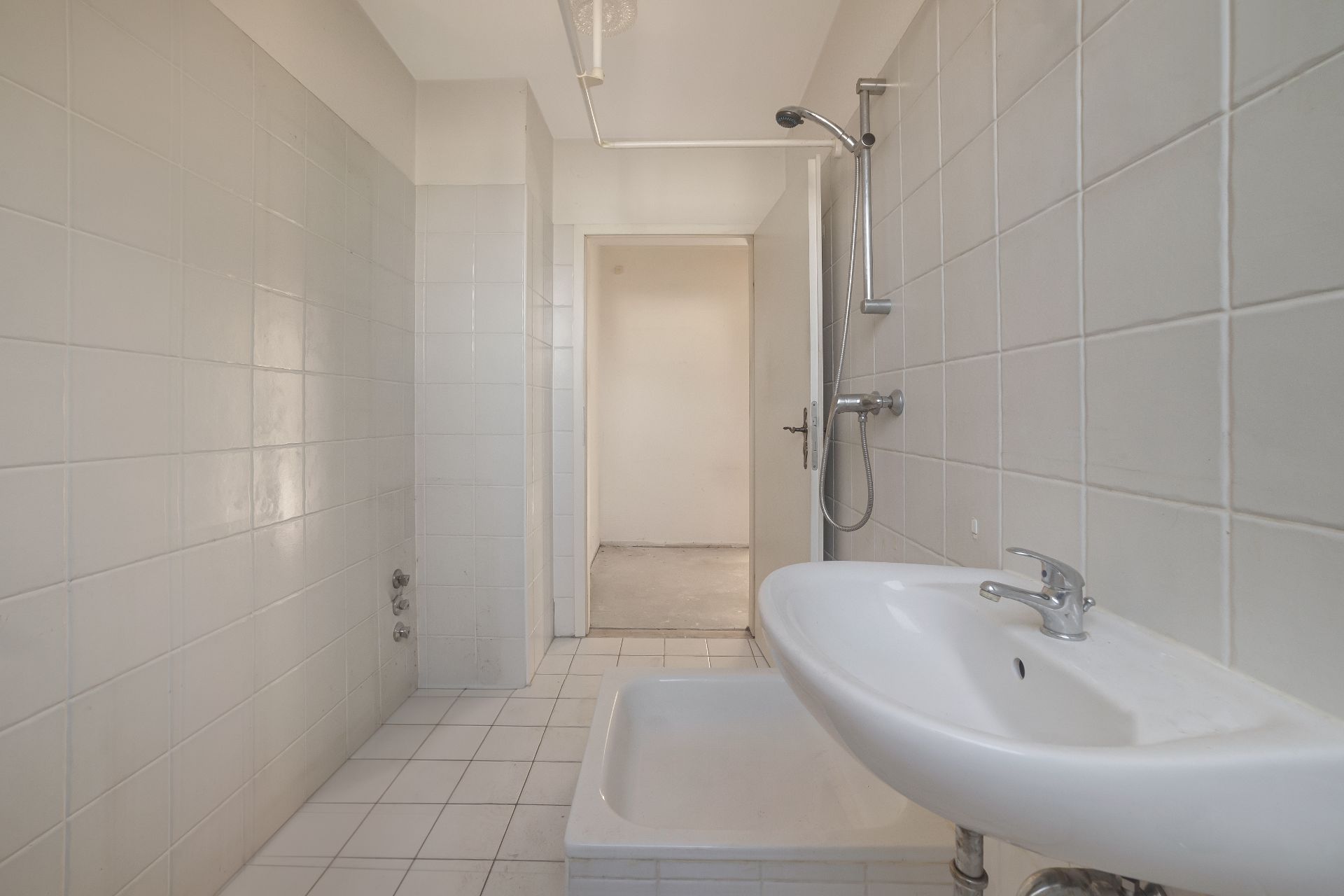 Helles Badezimmer mit Waschbecken, Dusche und weißen Fliesen an Wand und Boden.