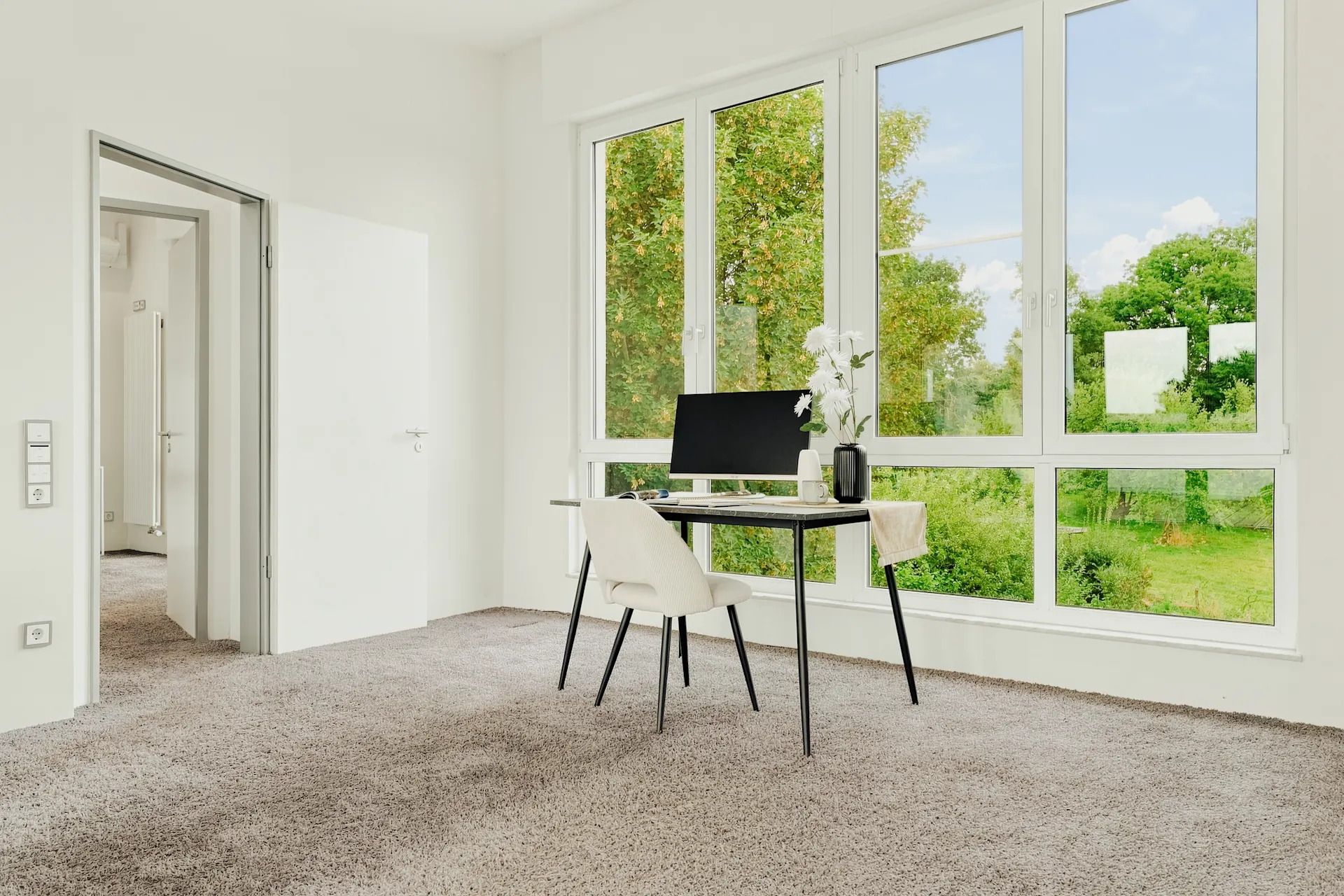 Helles Arbeitszimmer mit Schreibtisch, Stuhl und großem Fenster mit Blick ins Grüne.