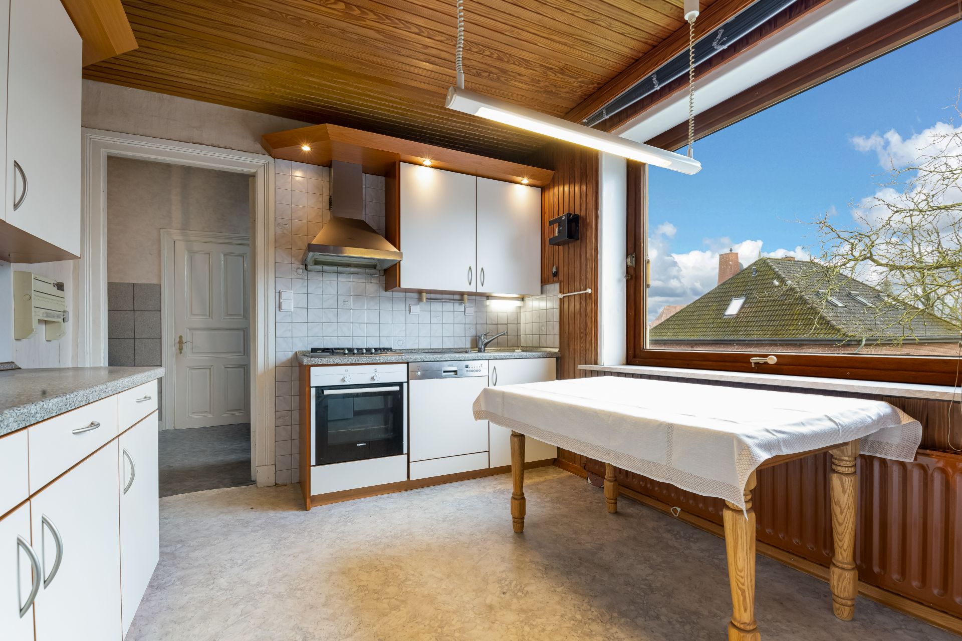 Helle Küche mit Holztisch, weißen Schränken und großem Fenster mit Blick nach draußen.