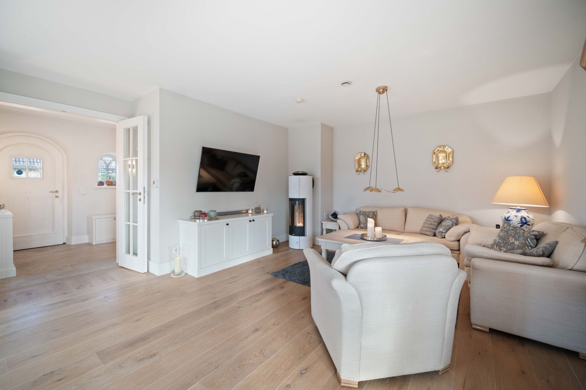 Helles Wohnzimmer mit Ecksofa, zwei Sesseln, Fernseher, Stehlampe und Holzfußboden.