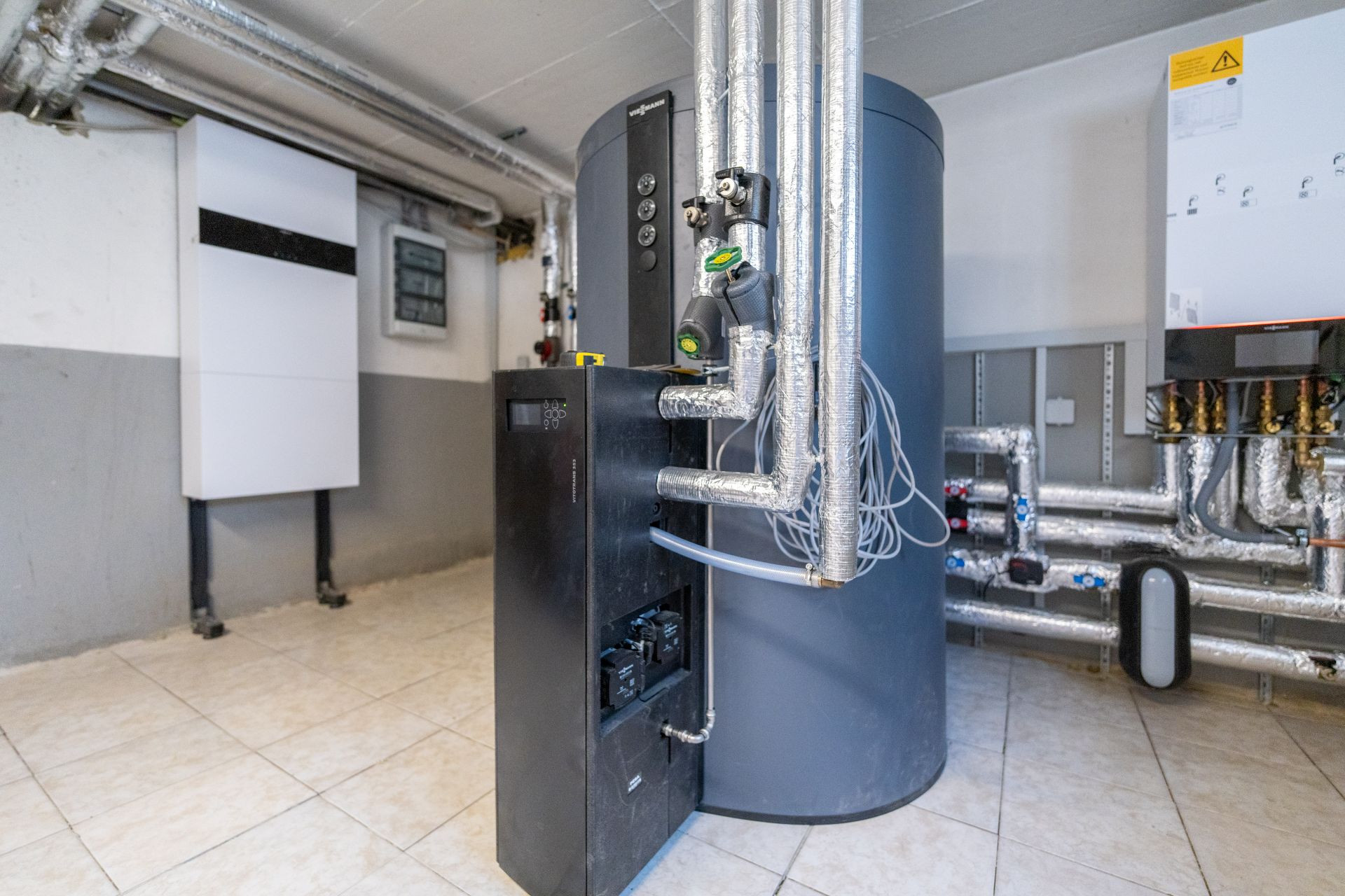 Heizungsraum mit moderner Heizungsanlage und mehreren isolierten Rohrleitungen.