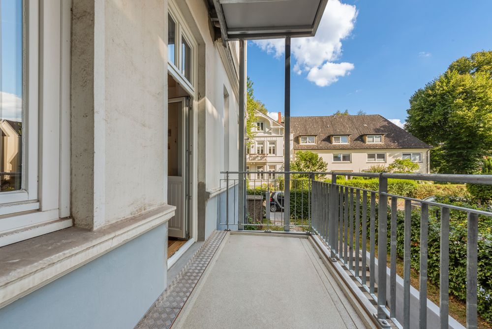 Balkon mit Geländer an einem Wohnhaus, Blick auf Nachbarhäuser und Garten.