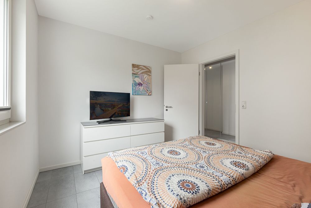 Schlafzimmer mit Bett, Kommode, Fernseher und offenem Fenster.