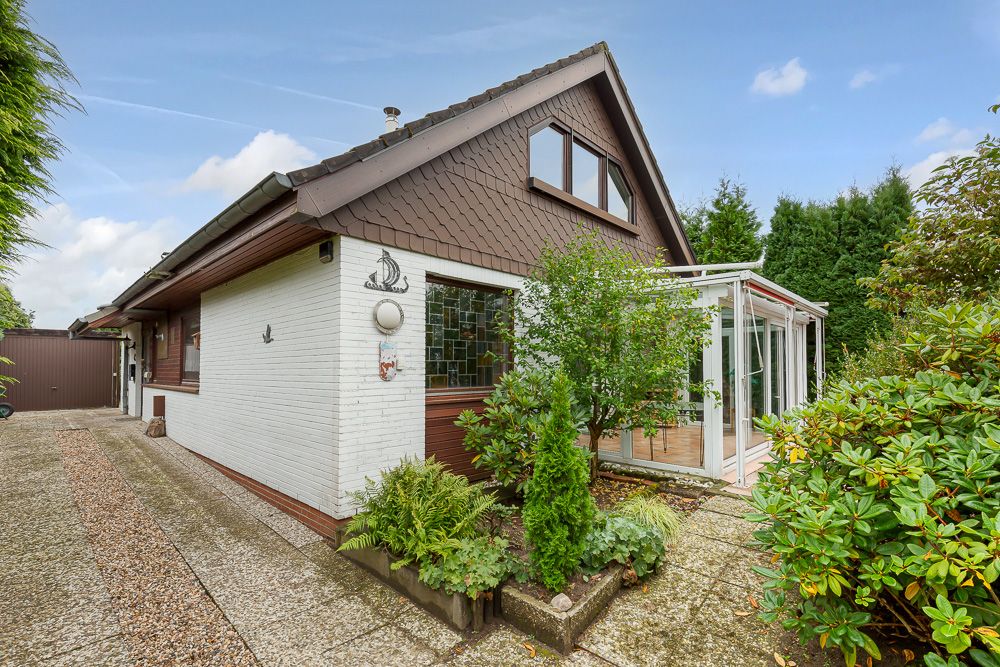 Einfamilienhaus mit Wintergarten, Garten und Kiesweg seitlich am Haus.