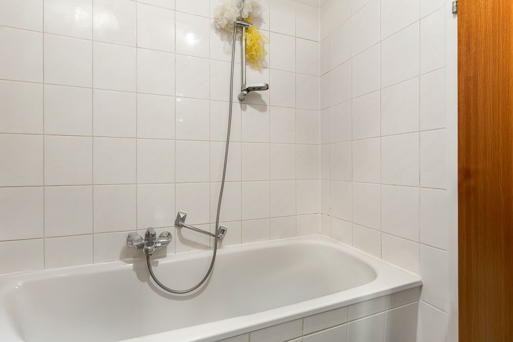 Weiße Badewanne mit Duschbrause und weiß gefliester Wand in einem Badezimmer.