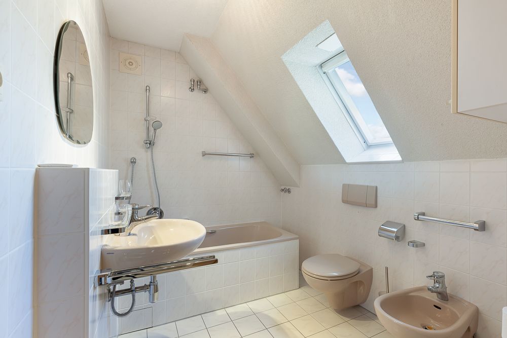 Helles Badezimmer mit Badewanne, Waschbecken, WC, Bidet und Fenster im Dach.