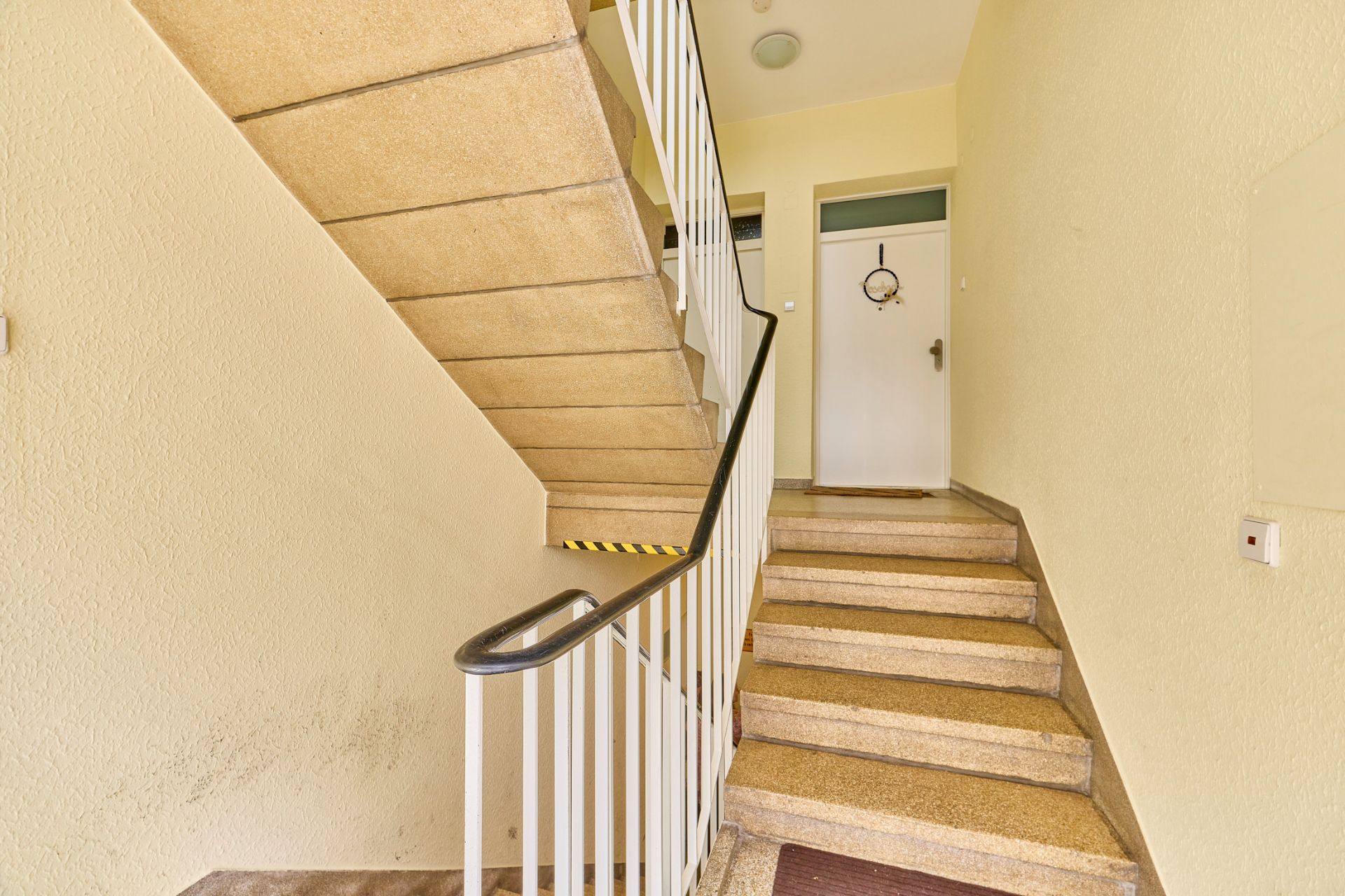 Treppenhaus mit Handlauf und Wohnungstür in einem Wohngebäude.