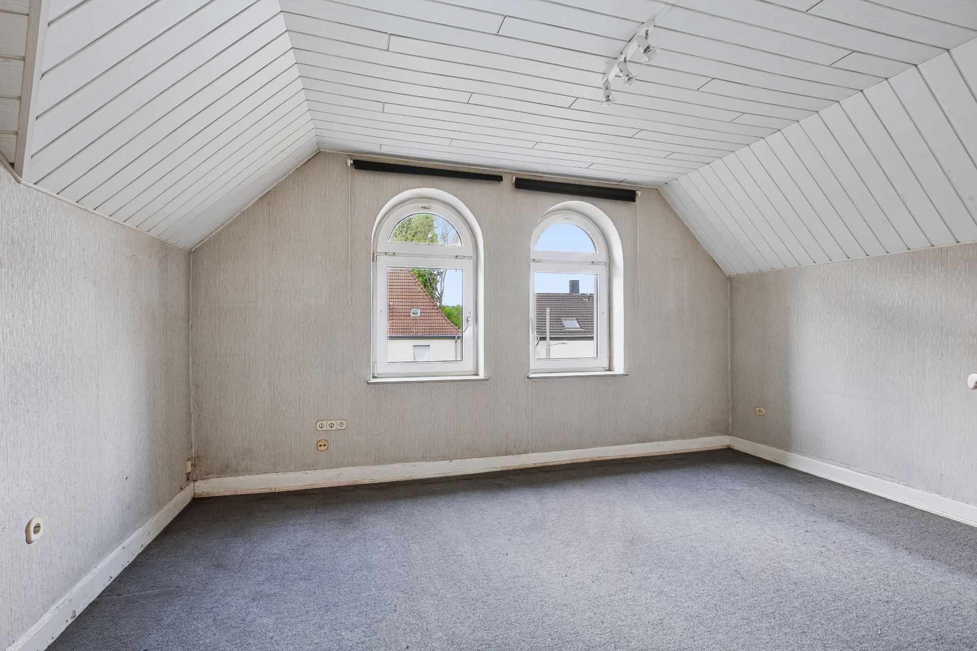 Leeres Zimmer mit schräger Decke und zwei großen Rundbogenfenstern.