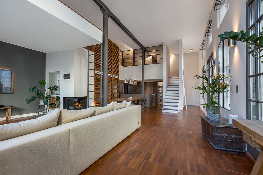 Großes, modernes Wohnzimmer mit Sofa, Holzboden, Kamin, Pflanzen und offener Treppe.