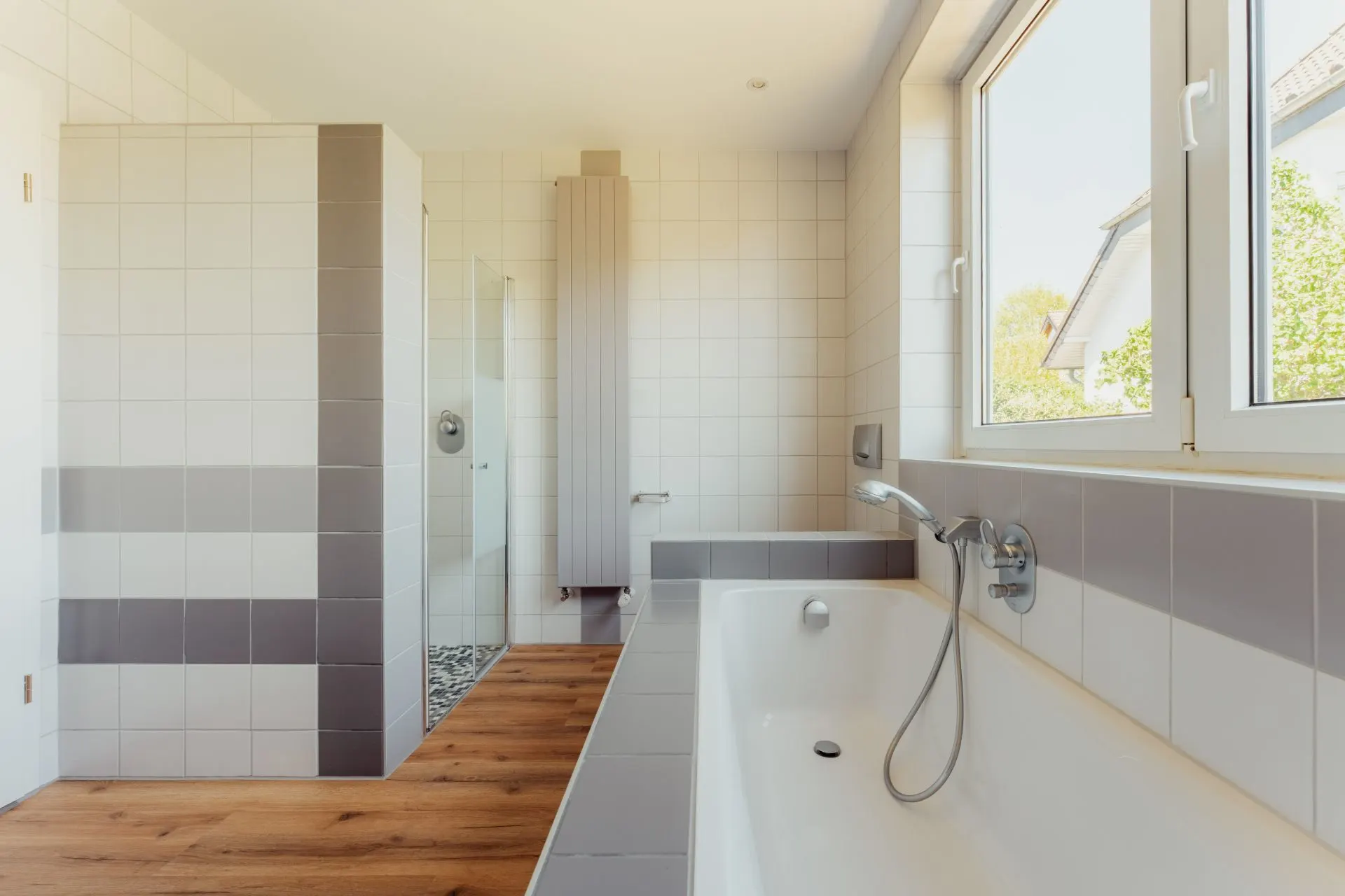 Modernes Badezimmer mit Badewanne, Dusche, großem Fenster und Holzfußboden.