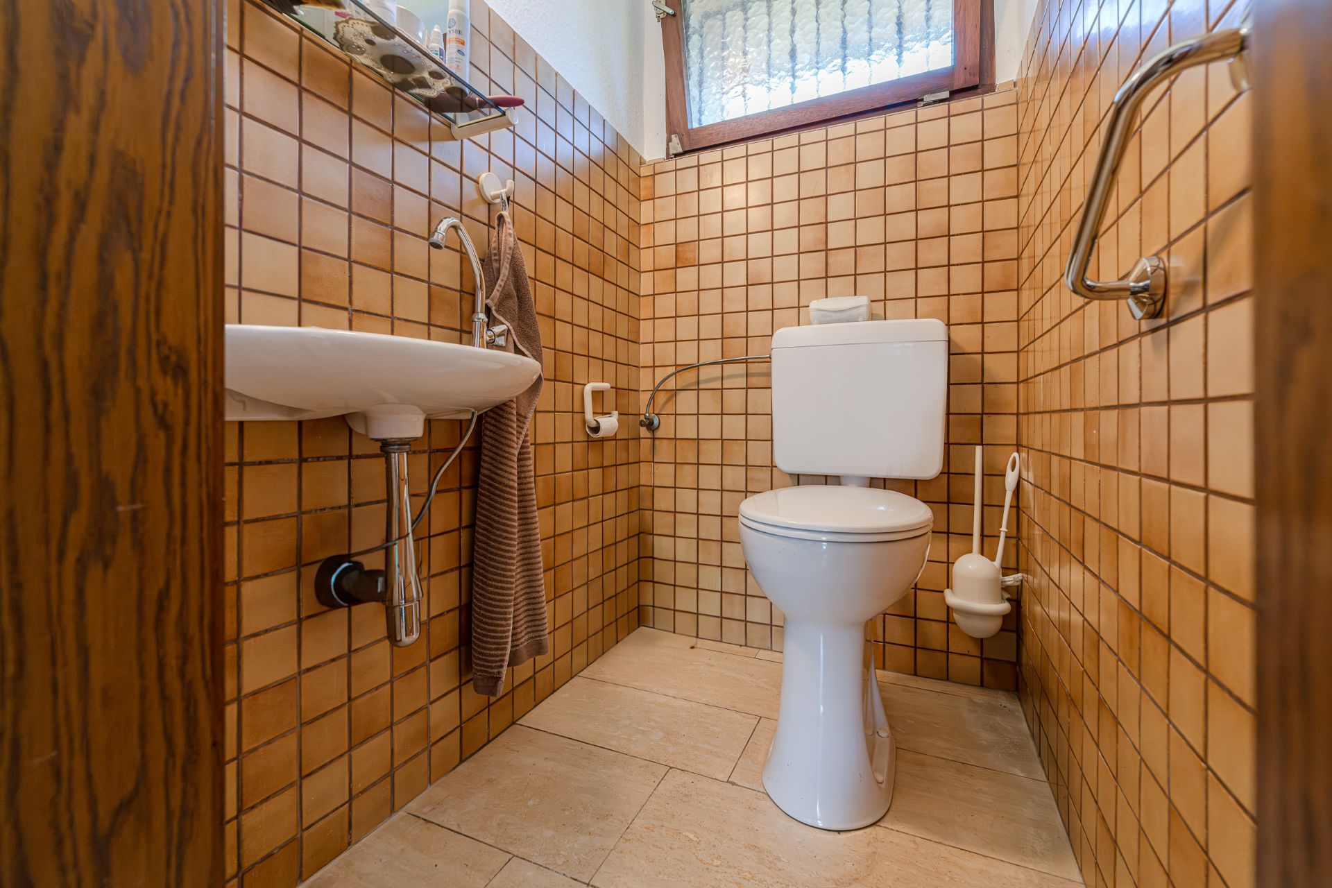 Kleines Badezimmer mit Toilette, Waschbecken und braunen Fliesen an den Wänden.