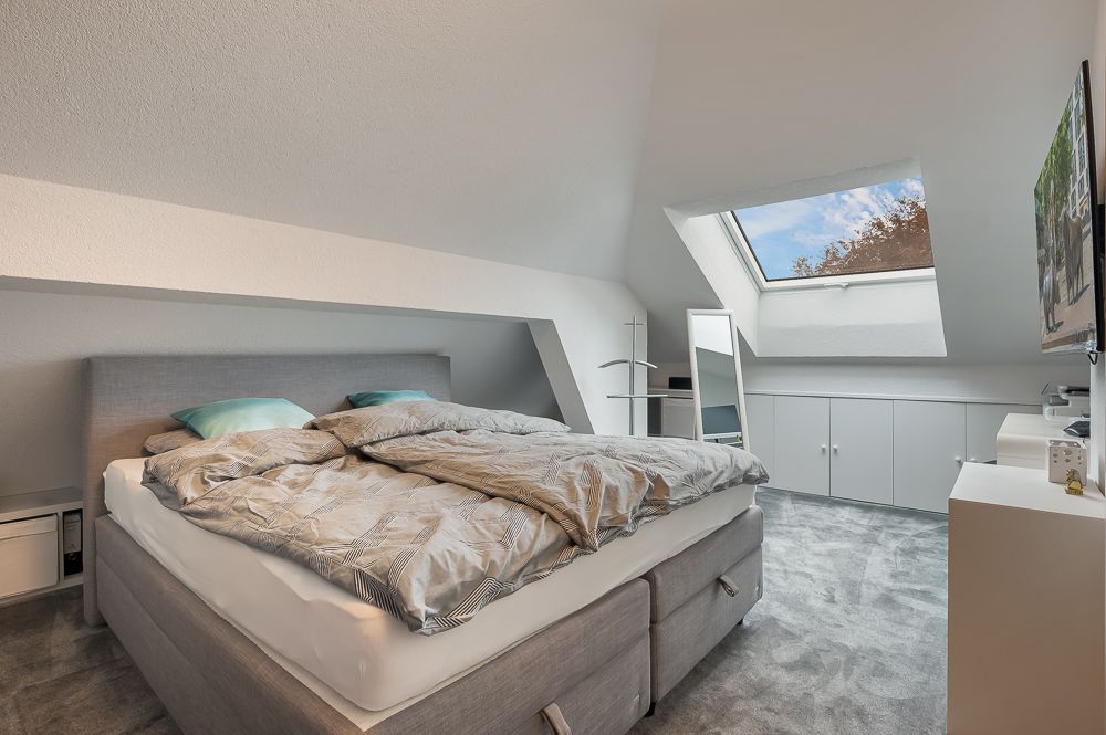 Schlafzimmer mit Doppelbett, Dachschräge, Teppichboden und großem Dachfenster.