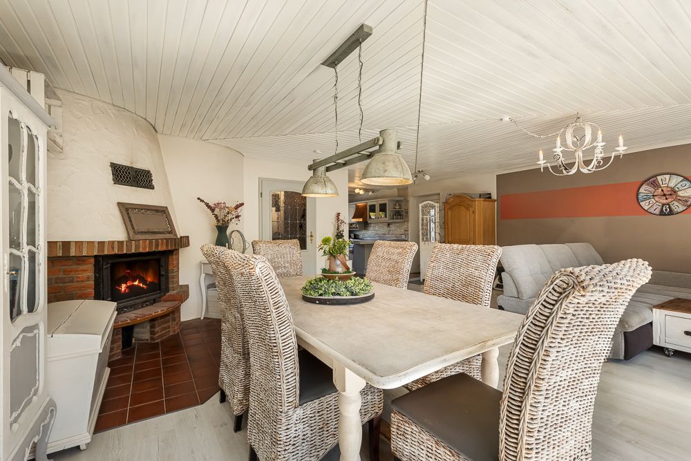 Esszimmer mit großem Tisch, Korbstühlen, offenem Kamin und Blick ins Wohnzimmer.