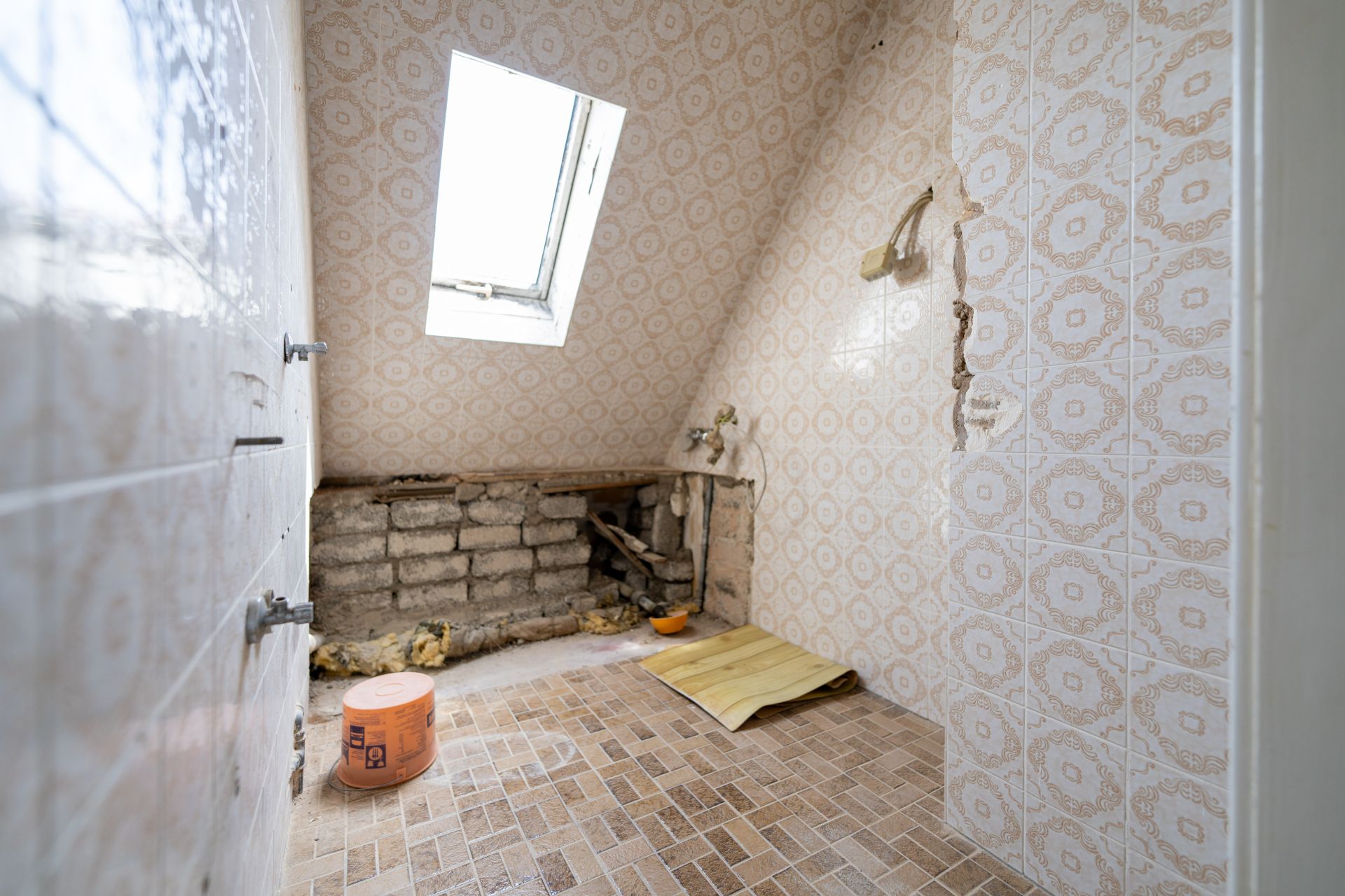 Renovierungsbedürftiges Bad mit schräger Decke, Dachfenster und freigelegter Wand.