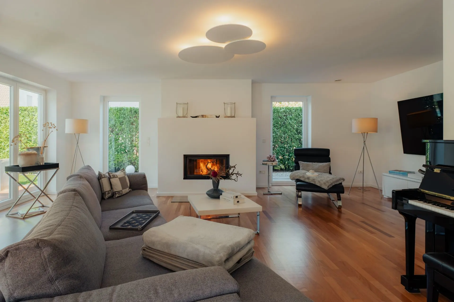 Helles Wohnzimmer mit Kamin, Sofa, Sesseln, Klavier und Holzboden.