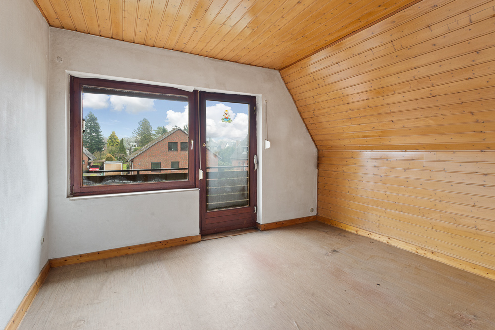 Leeres Zimmer mit Holzdecke und -wand, großer Fensterfront und Tür zum Balkon.