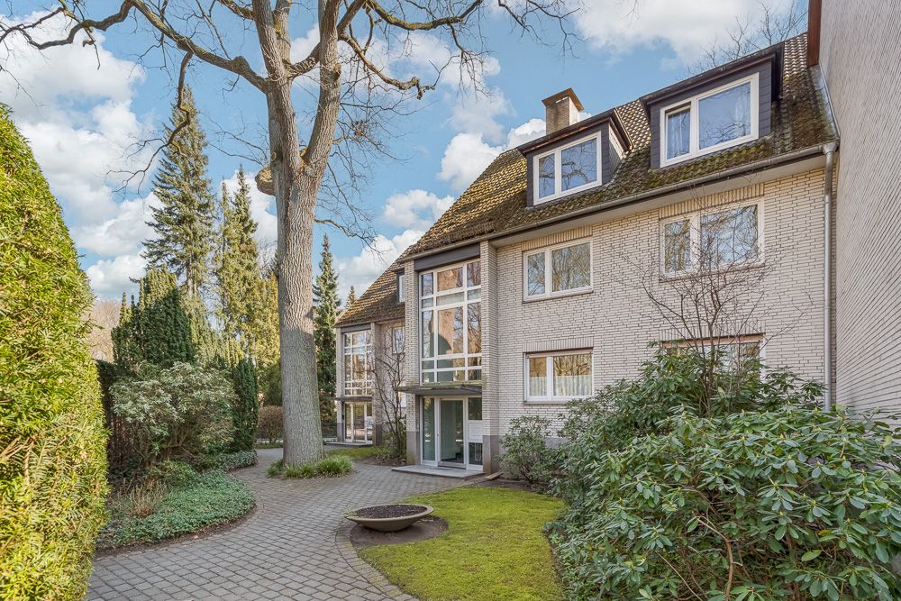 Mehrfamilienhaus mit hellem Eingangsbereich, umgeben von Bäumen und gepflegtem Garten.