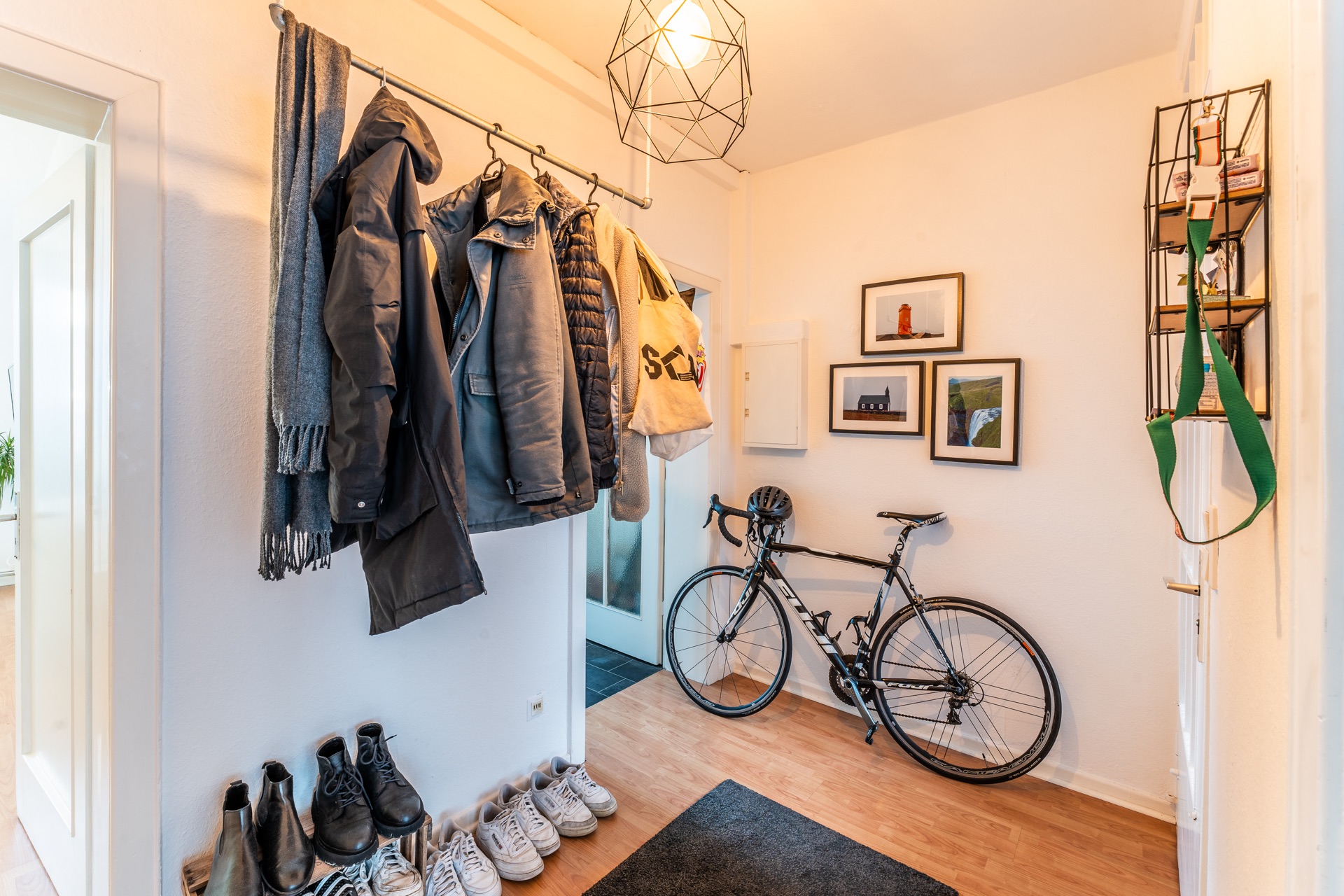 Flur mit aufgehängten Jacken, Schuhen am Boden, Fahrrad an der Wand und Bildern an der Wand.