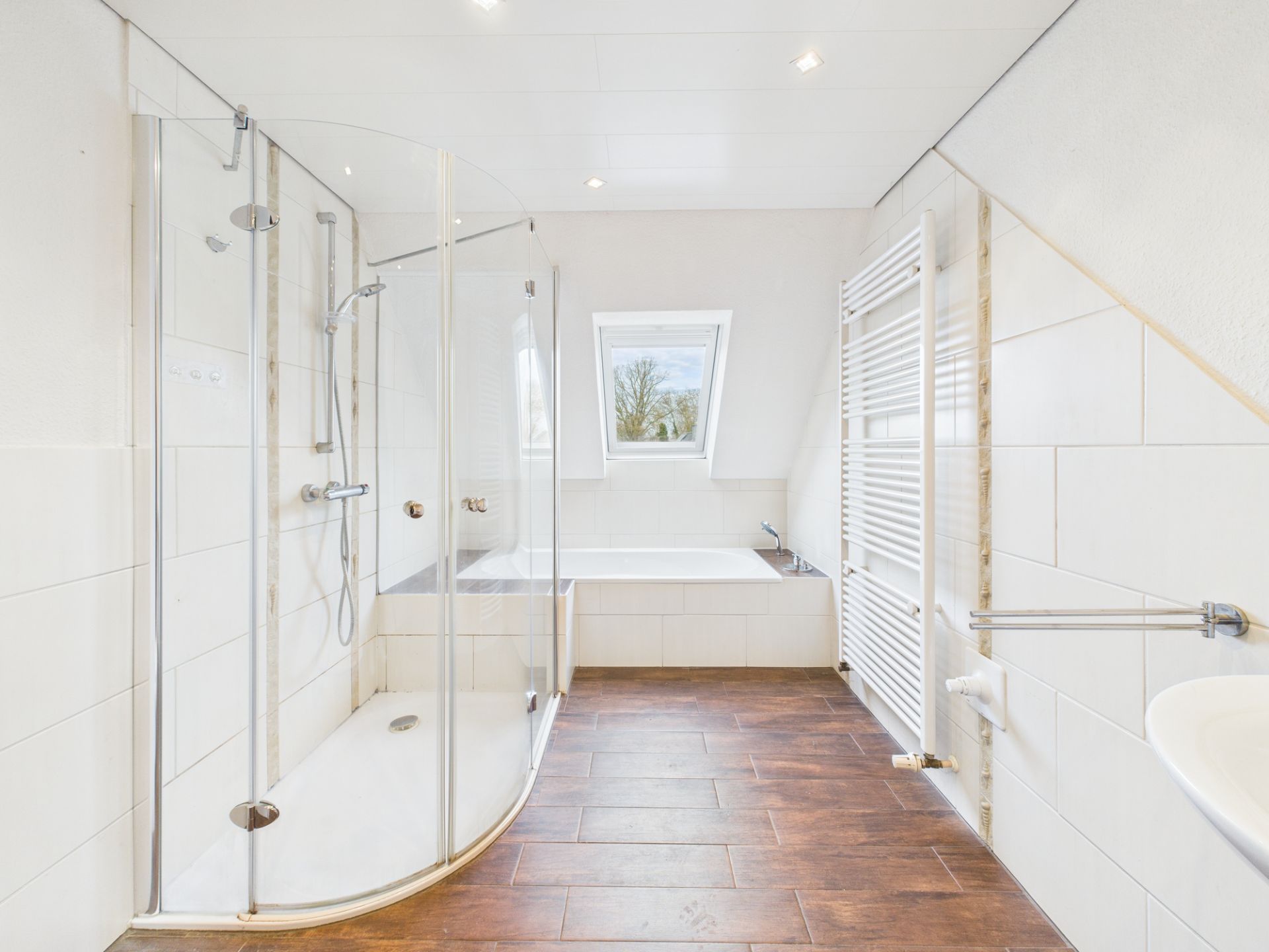 Modernes Badezimmer mit Glasdusche, Badewanne, Handtuchheizkörper und Fenster.