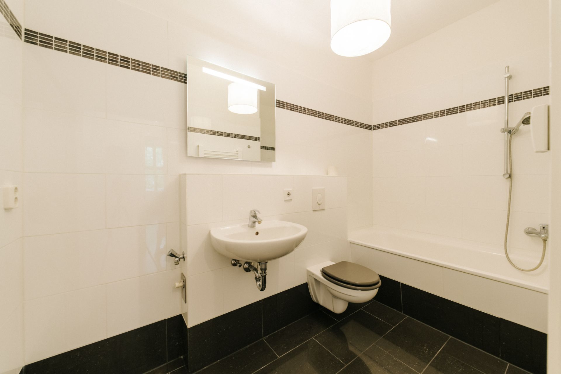 Helles Badezimmer mit Waschbecken, Spiegel, Toilette und Badewanne mit Duschbrause.