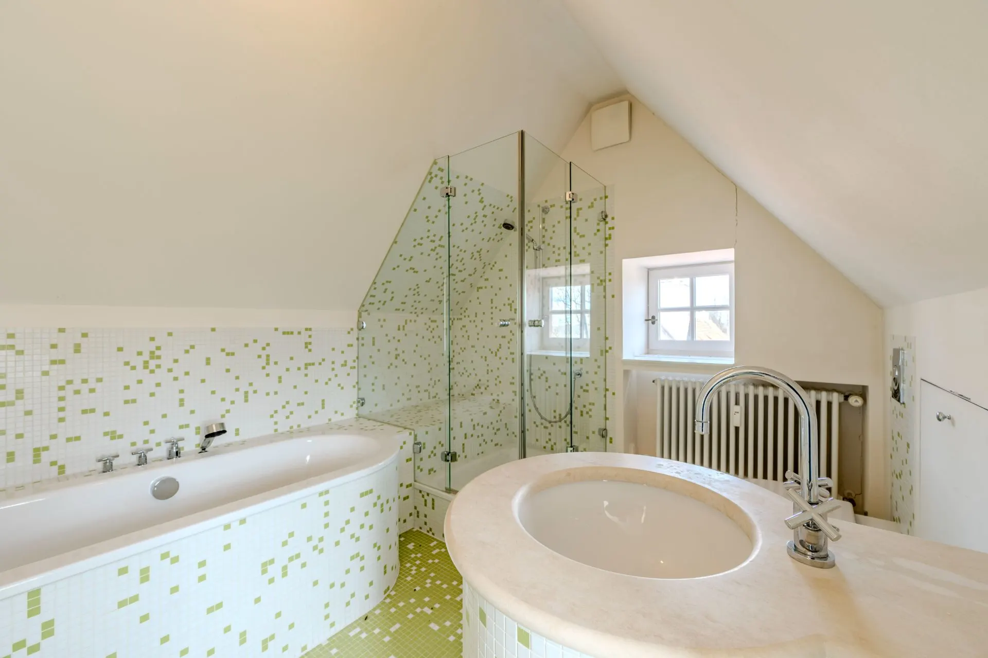 Modernes Badezimmer mit Badewanne, Dusche, Waschbecken und kleinem Fenster unter Dachschräge.