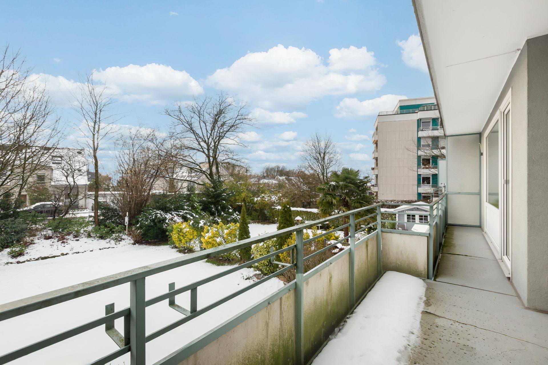 Balkon mit Schnee und Blick auf einen winterlichen Garten und Nachbargebäude.