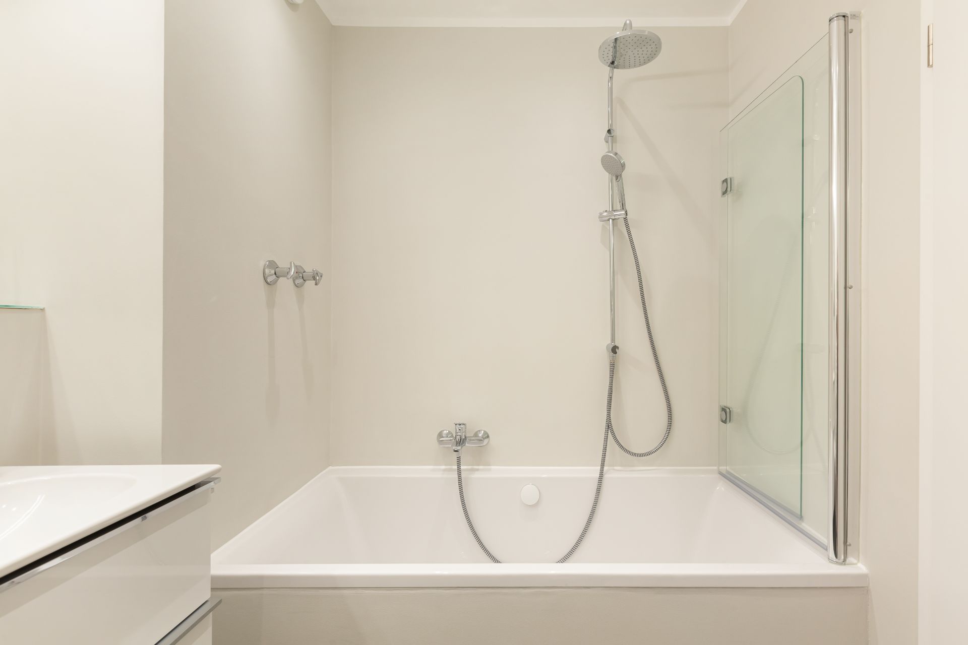 Helles Badezimmer mit Badewanne, Duschkopf und Glas-Duschabtrennung.
