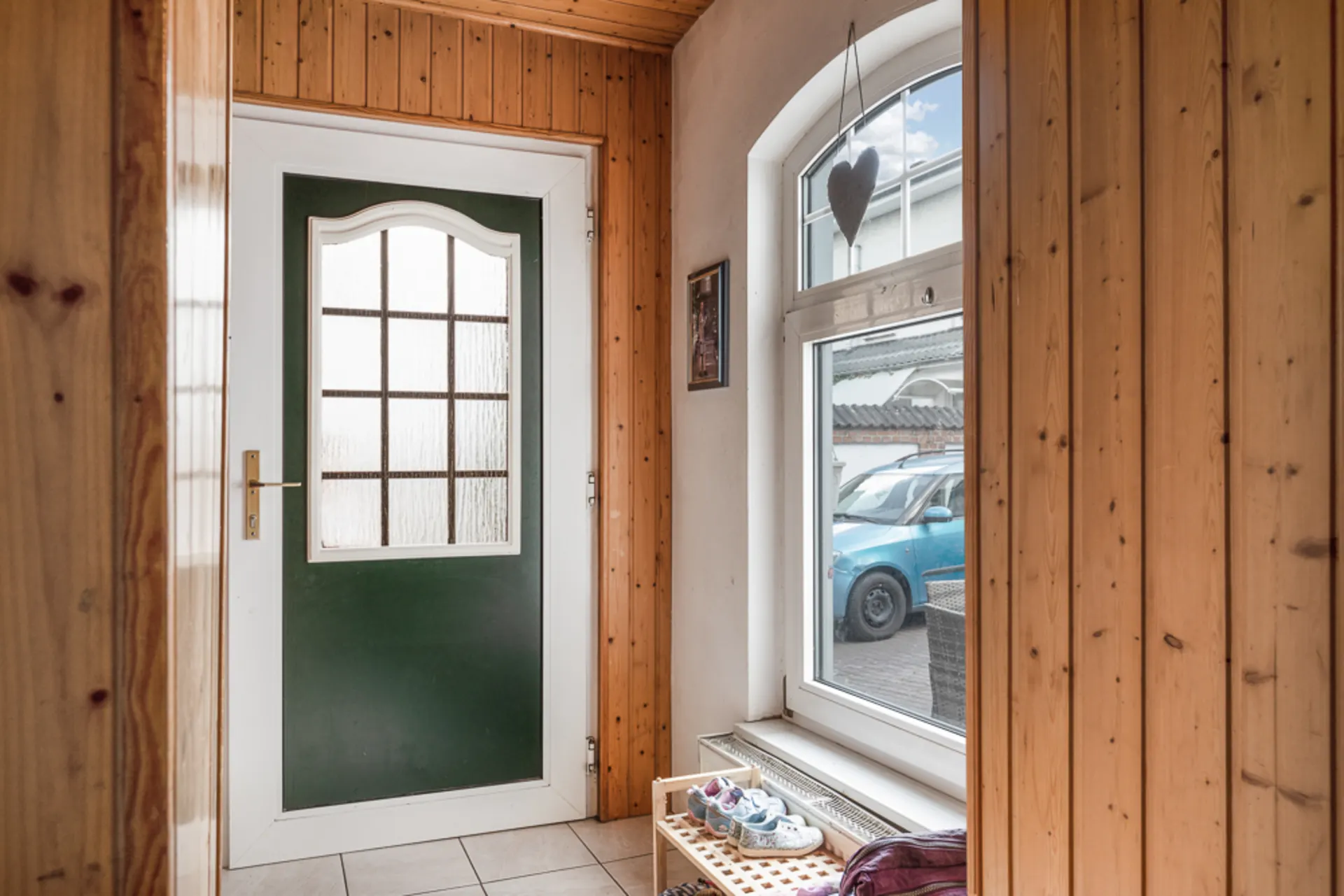 Eingangsbereich mit Holzwänden, weißer Tür, Fenster und einem Schuhregal mit Schuhen.