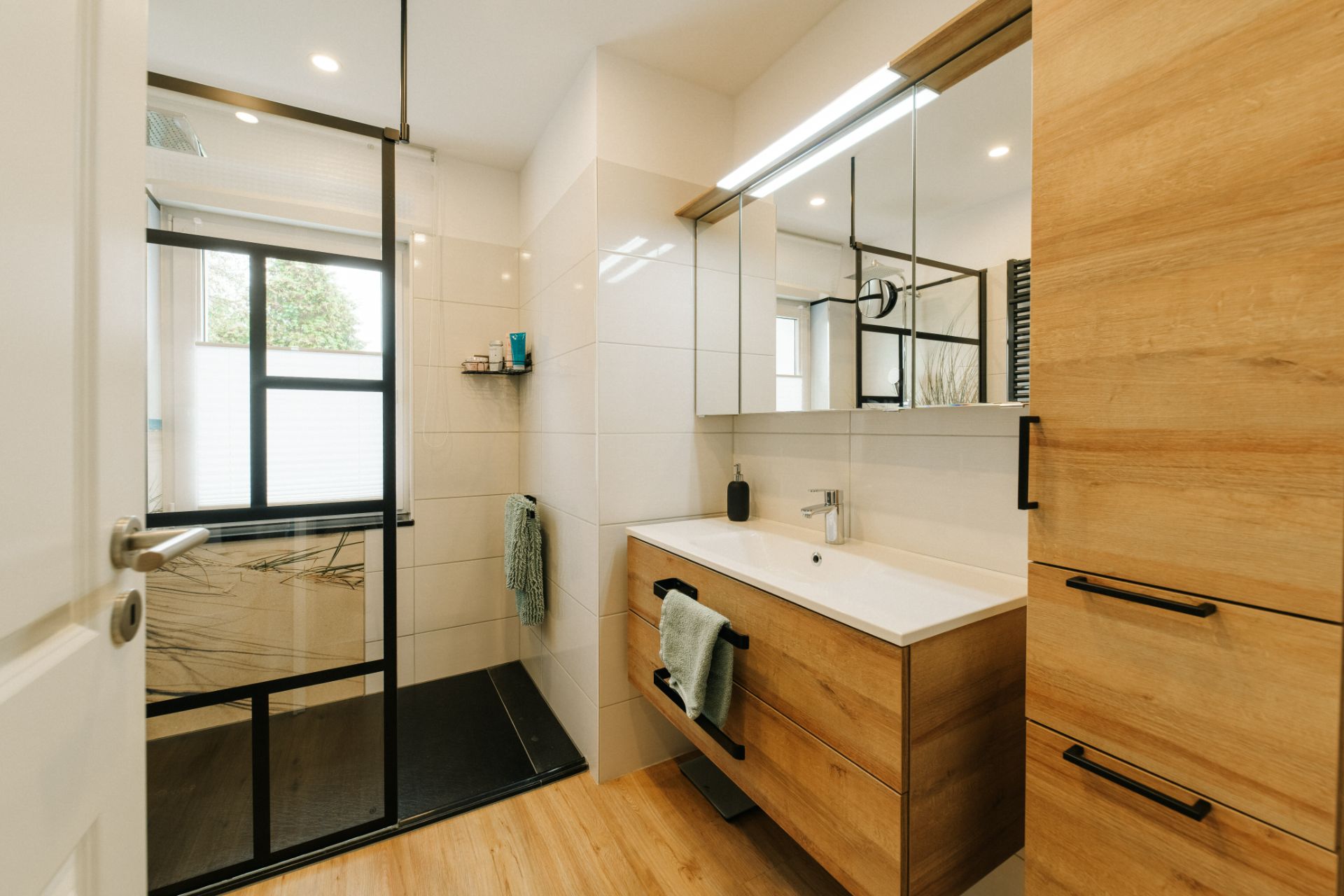 Modernes Badezimmer mit Holzschränken, großem Spiegel und begehbarer Dusche mit Glaswand.