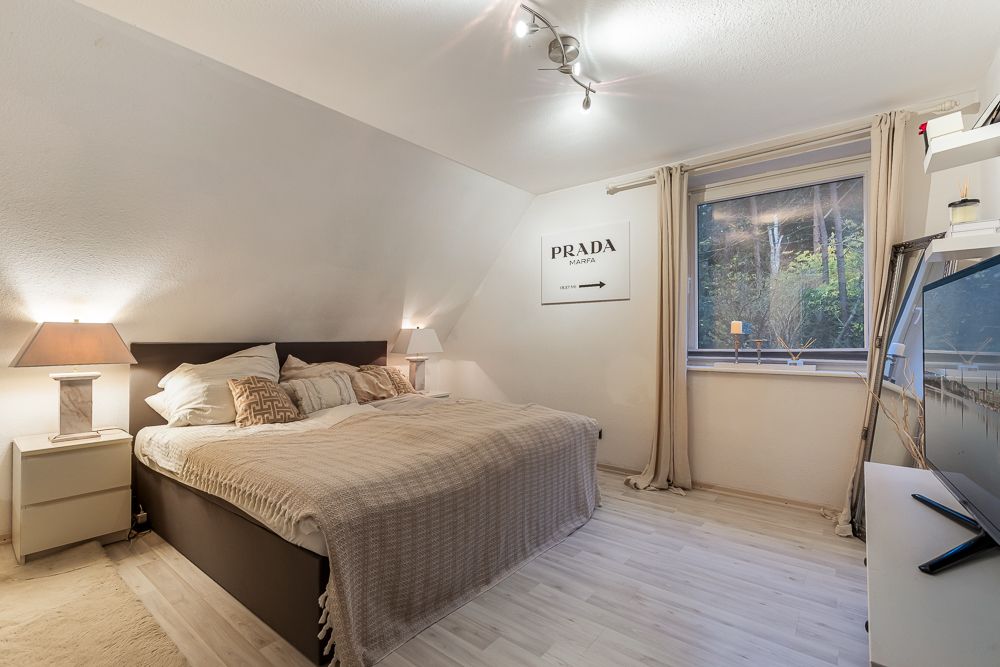 Helles Schlafzimmer mit Doppelbett, Nachttischen, Lampe, großem Fenster und Fernseher.