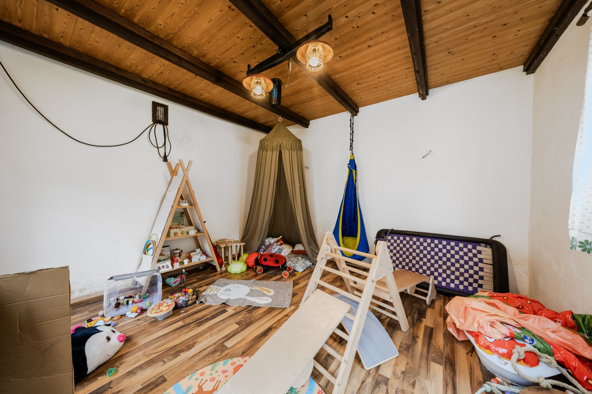 Kinderzimmer mit Spielzeug, Holzmöbeln, Tipizelt und Schaukel auf Holzfußboden.