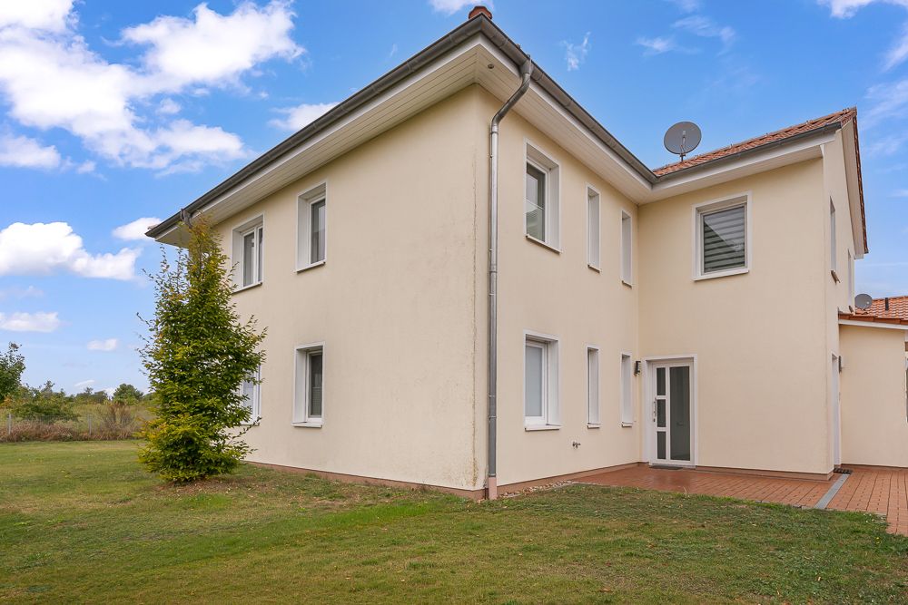 Zweistöckiges, cremefarbenes Wohnhaus mit vielen Fenstern und kleinem Garten.