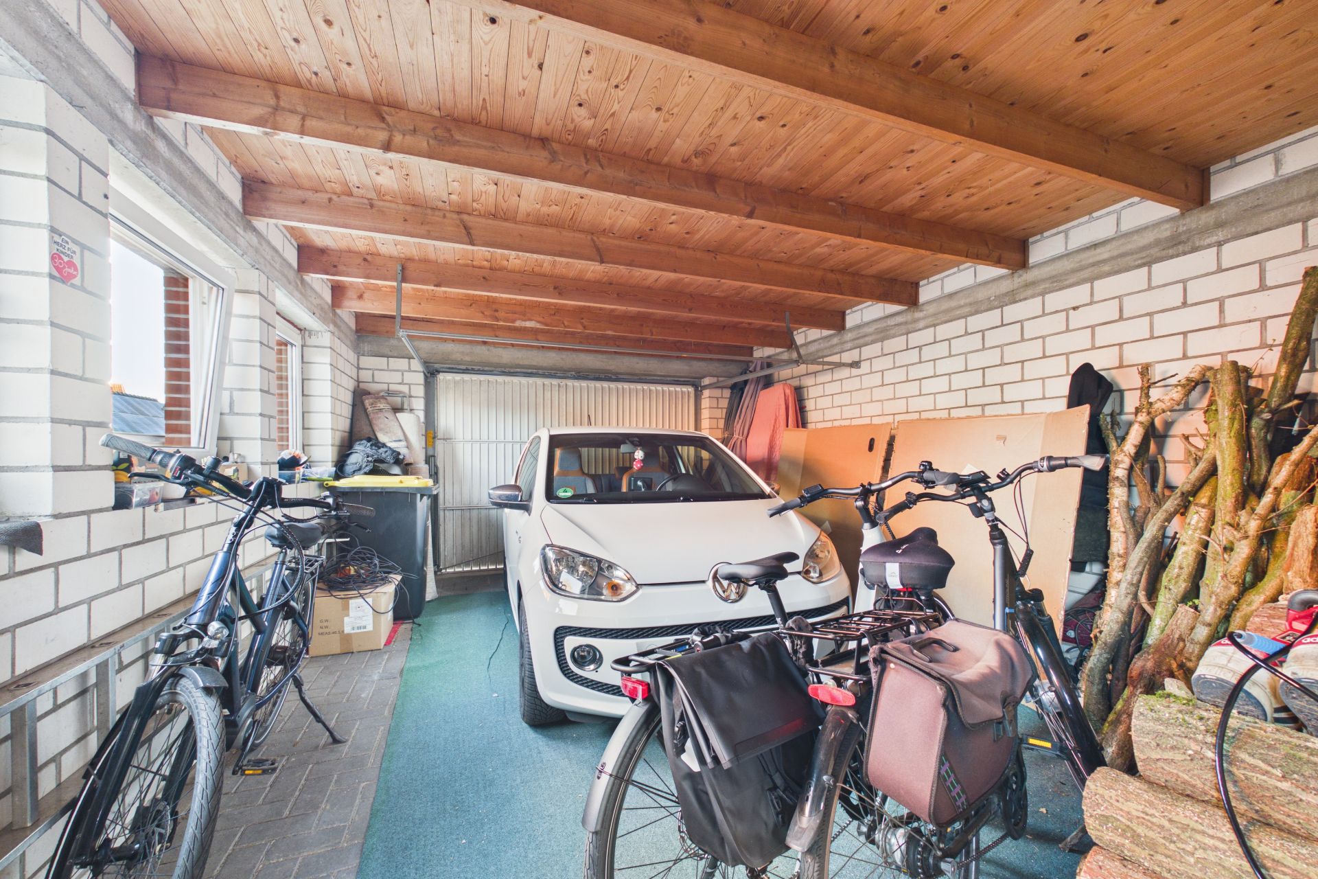 Garage mit einem weißen Auto, zwei Fahrrädern und gestapeltem Holz.