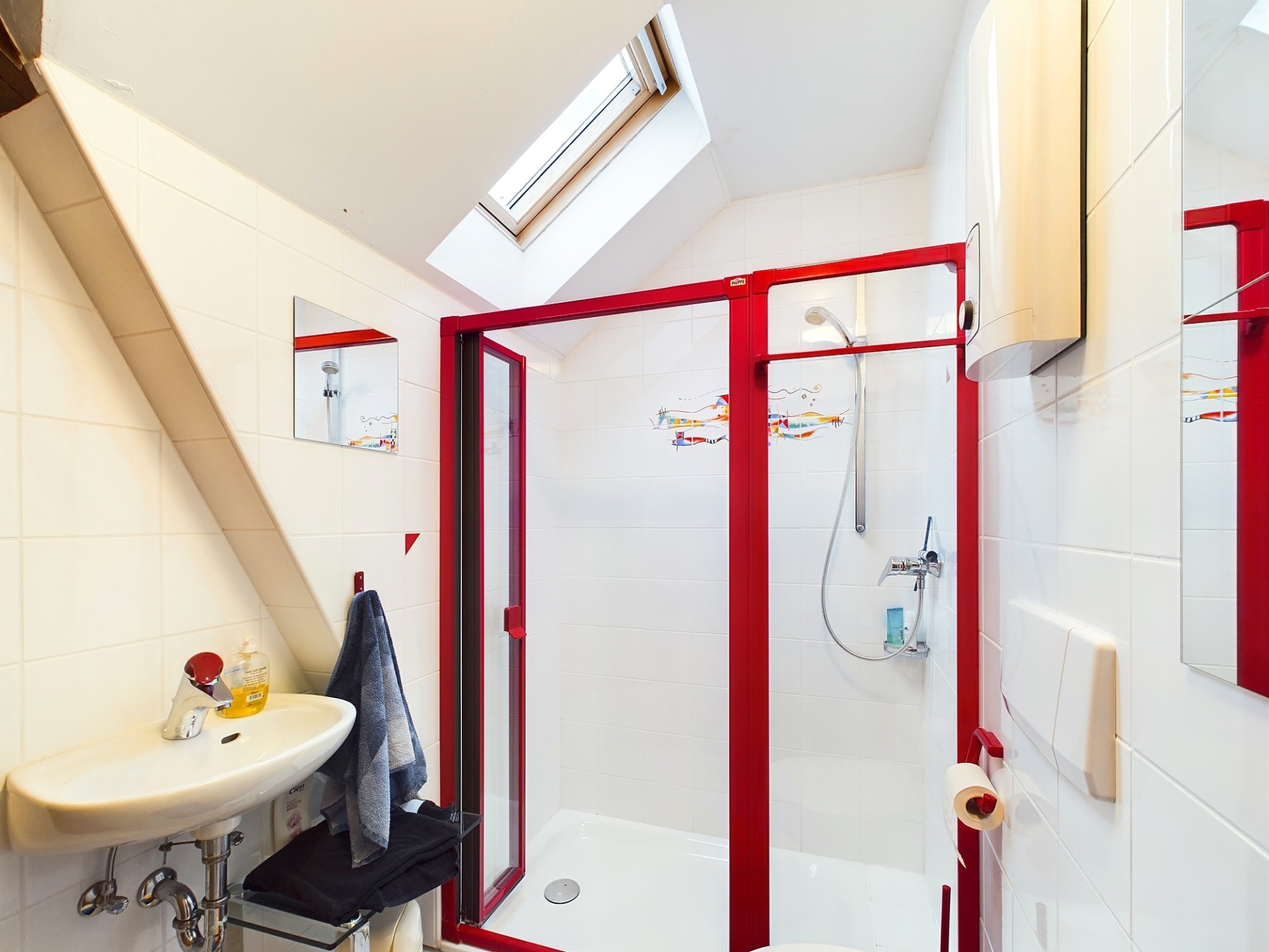 Modernes Badezimmer mit rotem Duschrahmen, Waschbecken, Spiegel und Dachfenster.