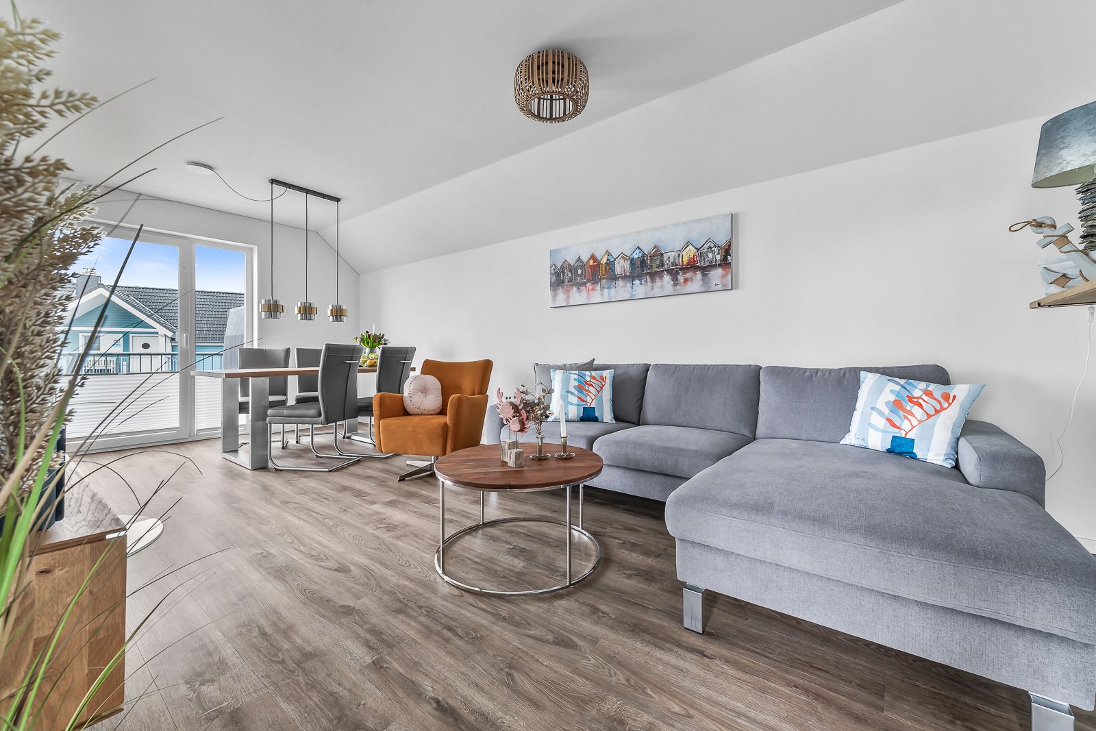 Modernes Wohnzimmer mit grauem Sofa, rundem Couchtisch und Essbereich am Fenster.