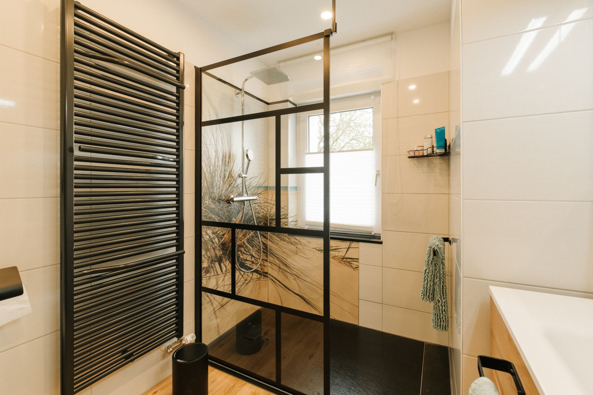 Modernes Badezimmer mit schwarzem Heizkörper, Glasduschwand und Fenster.