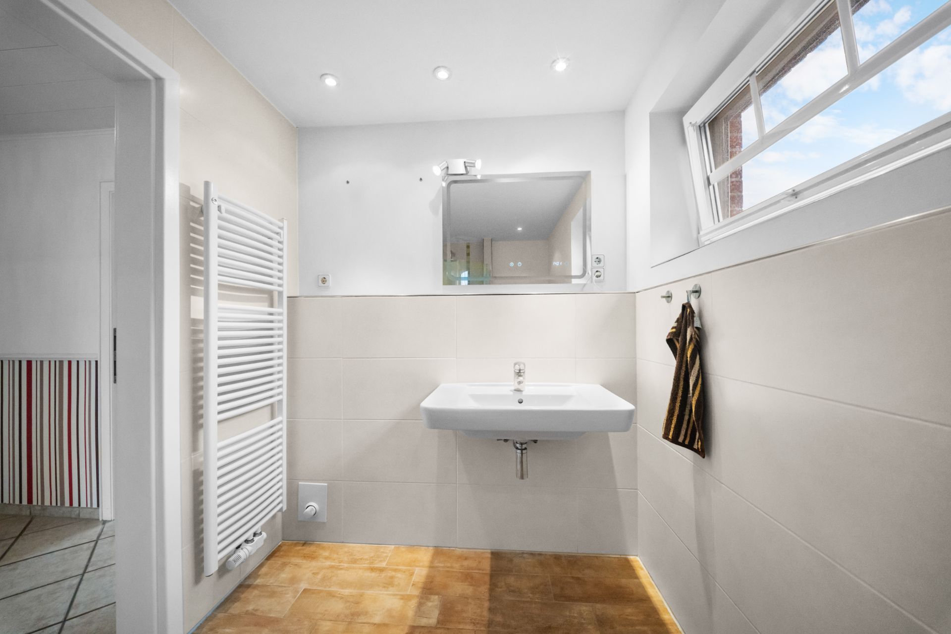 Helles Badezimmer mit Waschbecken, Spiegel, Handtuch und Fenster.