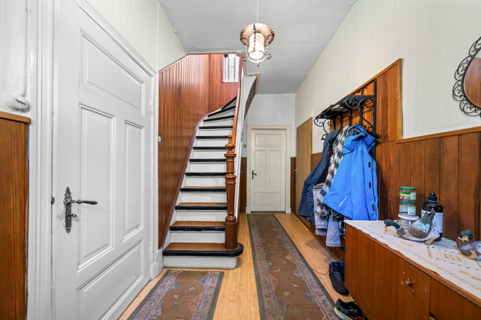 Hausflur mit Holztreppe, Garderobe, Teppichläufern und Kommode mit Dekorationen.