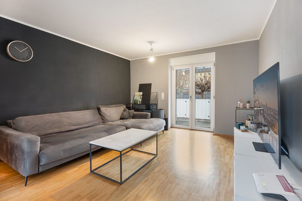 Modernes Wohnzimmer mit grauem Sofa, Couchtisch, Fernseher und Zugang zu einem Balkon.