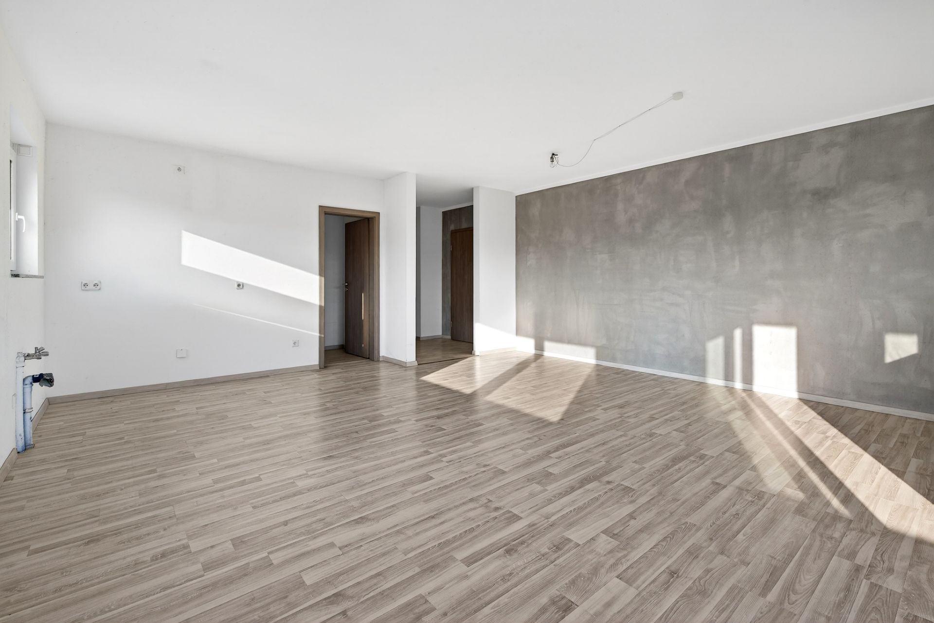 Heller leerer Raum mit Holzfußboden, weißen Wänden und einer grauen Akzentwand.