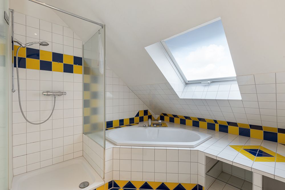 Badezimmer mit Badewanne, Dusche und Dachfenster. Bunte Fliesen in Blau und Gelb.