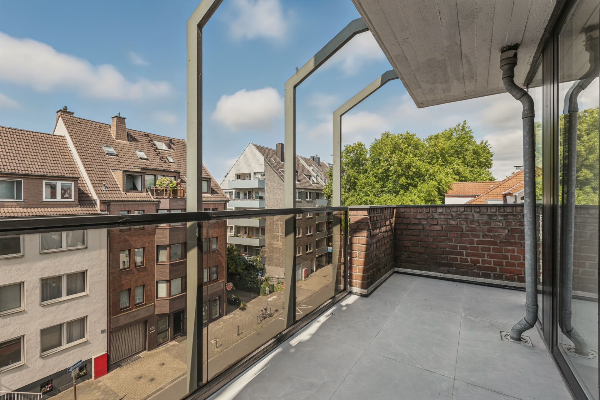 Balkon mit Glasgeländer, Blick auf Wohnhäuser und Bäume.