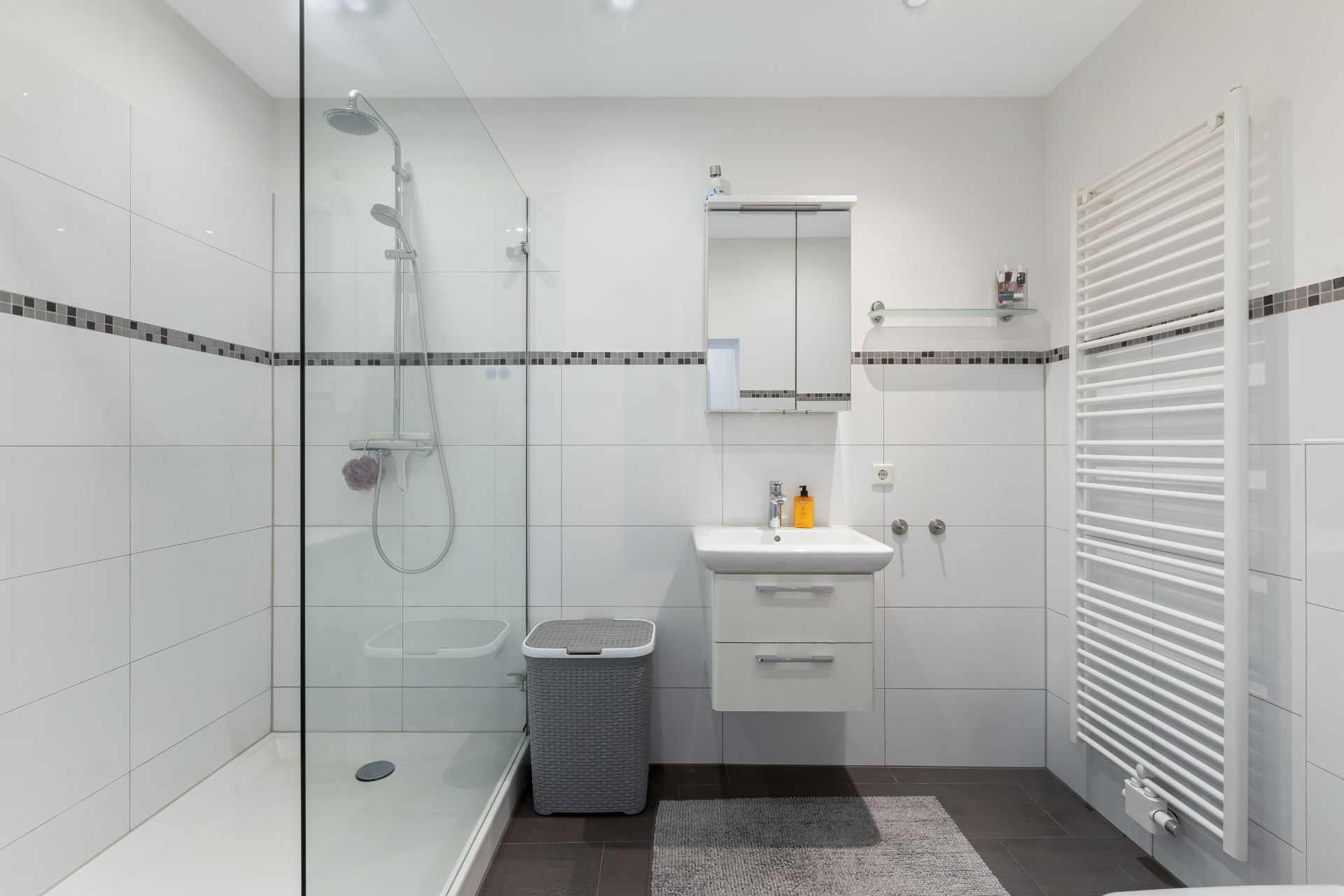Modernes Badezimmer mit Dusche, Waschbecken, Spiegel, Handtuchheizkörper und Wäschekorb.