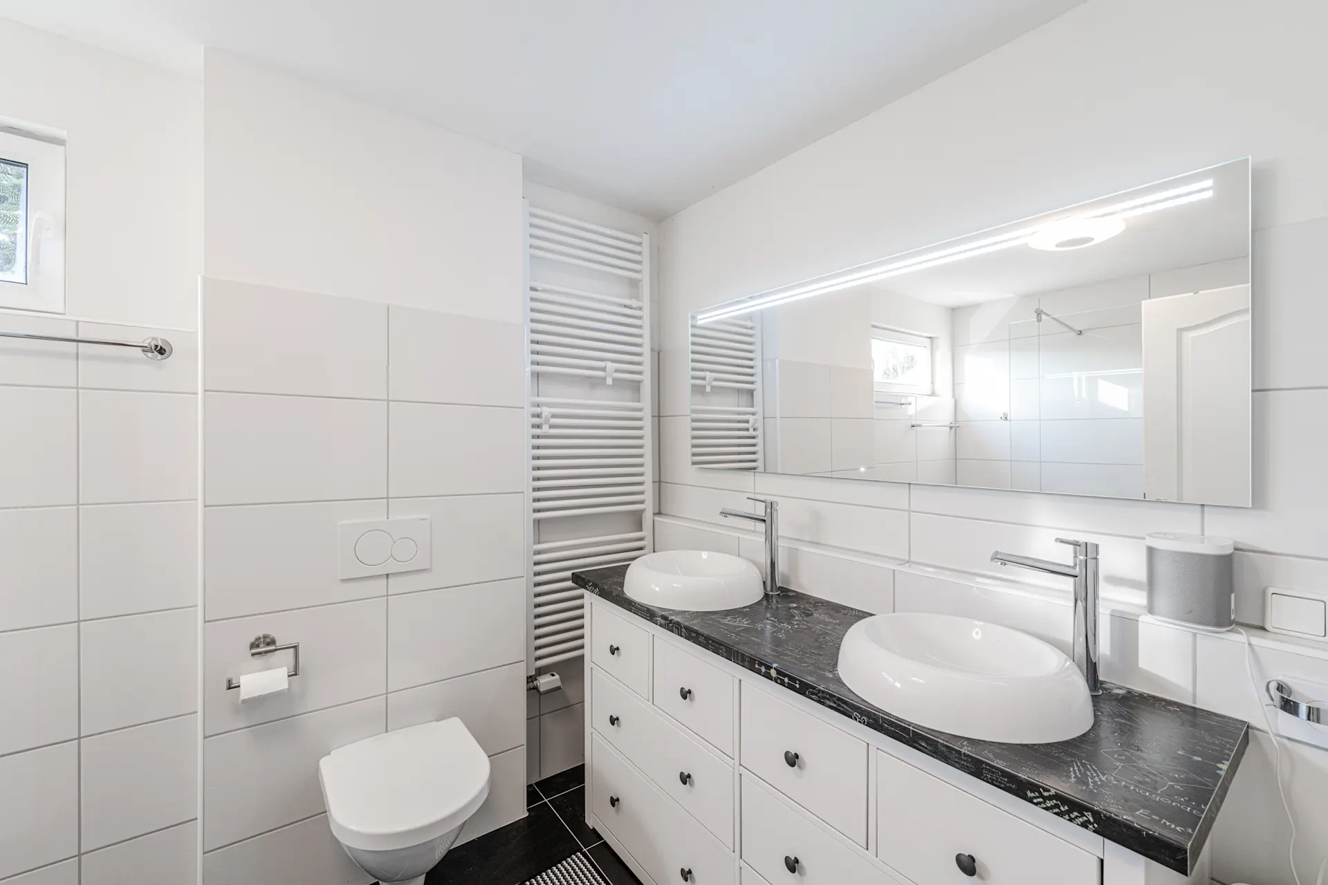 Modernes Badezimmer mit Doppelwaschbecken, großem Spiegel und Wandtoilette.