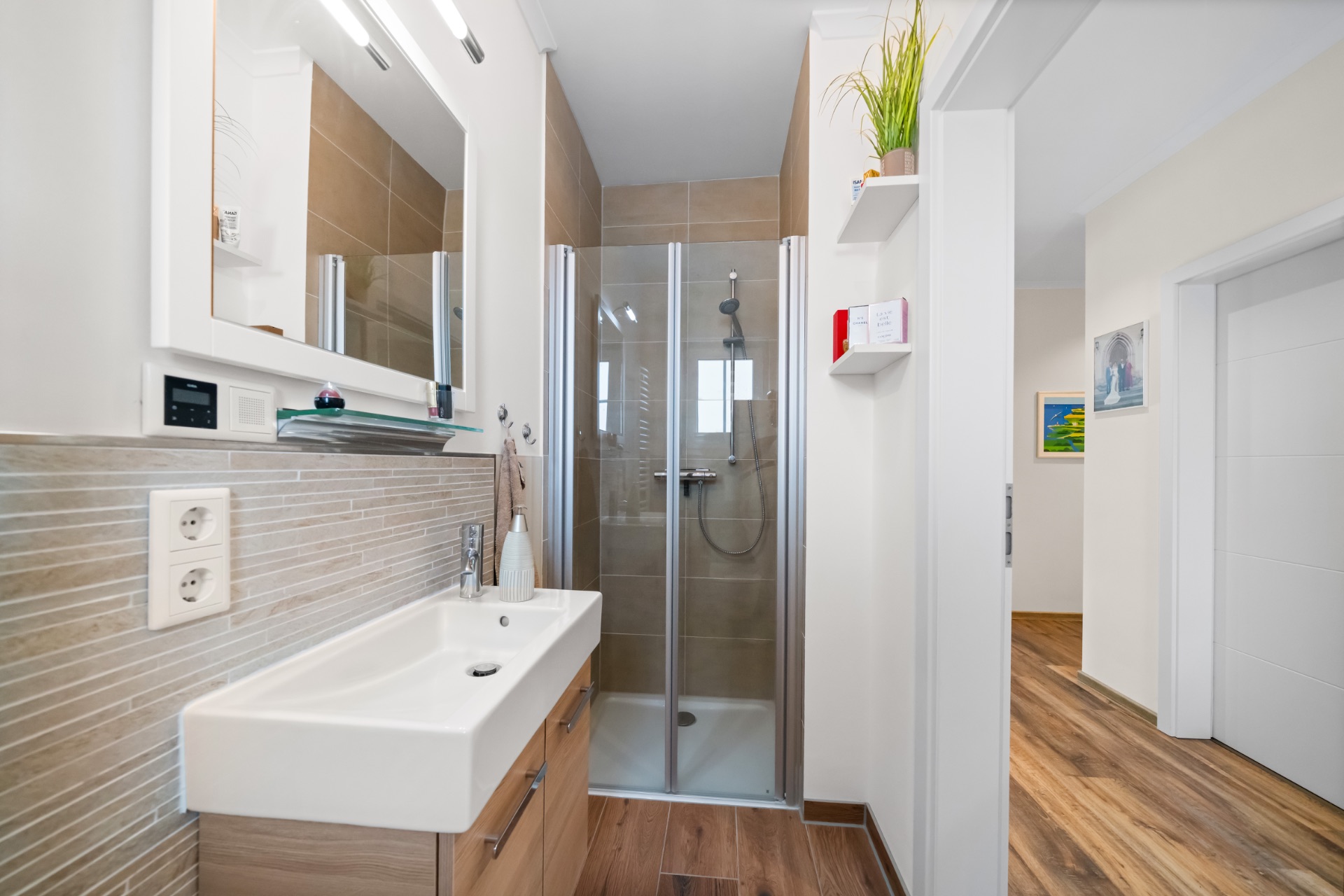 Modernes Bad mit Dusche, Waschbecken, Spiegel und Zugang zum Flur, Holzboden im Flur sichtbar.